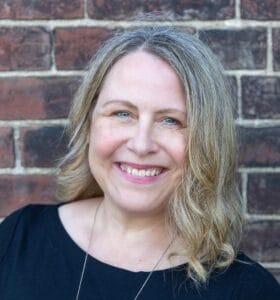 Woman with shoulder length hair smiling by brick wall